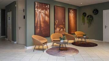 A modern lobby with three large wall-mounted deer paintings, a seating area with three chairs and a round table, and a tiled floor.