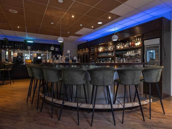 A bar area with a round bar and six stools, a counter with a cash register, and shelves with bottles and glasses.