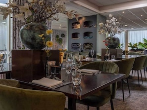 Een restaurant met een donker houten eettafel, omringd door groene bekleden stoelen.