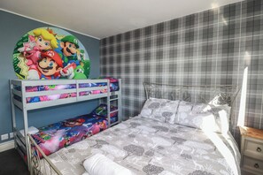 A bedroom with a bunk bed, a bed with patterned bedding, a wall clock, and a window with a view. - Shoreline Apartment No.8 (Newquay)