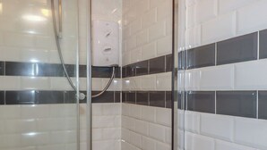 A shower enclosure with a glass door, white tiled walls, and a black and white tile pattern. - Shoreline Apartment No.8 (Newquay)