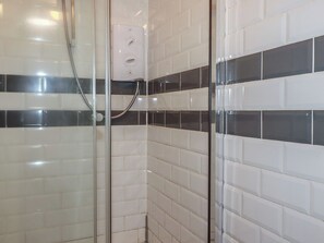 A shower enclosure with a glass door, white tiled walls, and a black and white tile pattern. - Shoreline Apartment No.8 (Newquay)