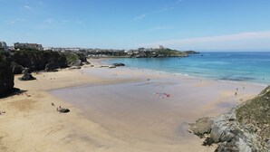 A coastal beach with clear skies, rocky outcrops, and a distant building on a hill. - Shoreline Apartment No.8 (Newquay)