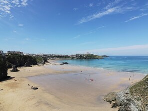 A coastal beach with clear skies, rocky outcrops, and a distant building on a hill. - Shoreline Apartment No.8 (Newquay)