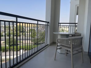 A balcony with a table and chairs, a view of a road and greenery, and a clear sky. - Serene Yas Island Hideaway w Resort Facilities (Abu Dhabi)