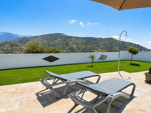 A terrace with two lounge chairs, a white wall with decorative elements, and a view of a mountainous landscape. - Cortijo Juan de Dios Piscina Privada en Competa (Còmpeta)