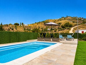 A swimming pool with lounge chairs and an umbrella, surrounded by a well-maintained lawn and a hillside in the background. - Cortijo Juan de Dios Piscina Privada en Competa (Còmpeta)