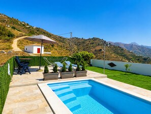 A swimming pool with a view of a hillside and a white building with a red door. - Cortijo Juan de Dios Piscina Privada en Competa (Còmpeta)