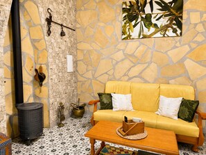 A cozy room with a stone wall, a yellow sofa, a wooden table, and a black heater. - Cortijo Juan de Dios Piscina Privada en Competa (Còmpeta)