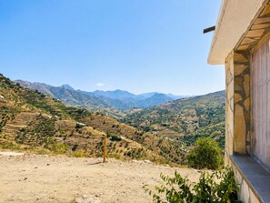 A mountainous landscape with terraced fields, a clear sky, and a building with a stone facade. - Cortijo Juan de Dios Piscina Privada en Competa (Còmpeta)