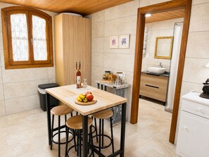 A modern kitchen with a wooden table, bar stools, a fruit bowl, and a bottle of wine. - Cortijo Juan de Dios Piscina Privada en Competa (Còmpeta)