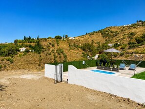 A pool area with a white wall, a gate, and a view of a hillside with houses. - Cortijo Juan de Dios Piscina Privada en Competa (Còmpeta)