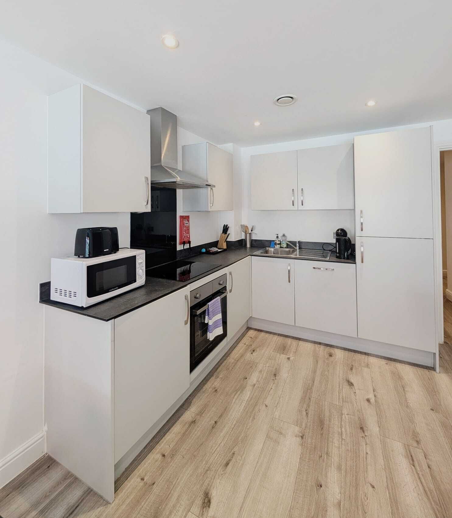 A modern kitchen with white cabinetry, a microwave, a stove, and a coffee maker.