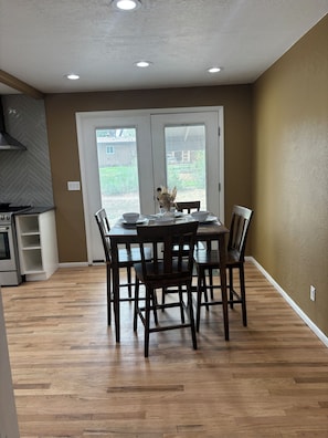 A dining area with a wooden table and chairs, a kitchen with a stove, and a view through a door to a backyard. - Lovely updated 3-bedroom house in quaint Cortez perfect for your getaway (Cortez)