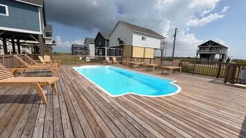 Una terraza de madera con piscina, sillas de descanso y vistas a casas.