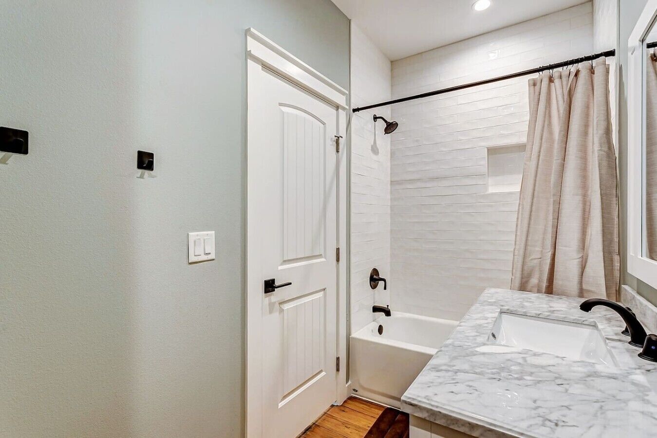 A bathroom with a white door, a bathtub, a shower, and a marble sink.