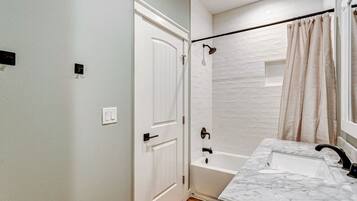Un baño con puerta blanca, bañera, ducha y lavamanos de mármol.