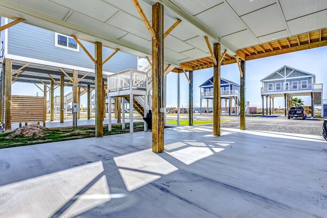 A covered outdoor area with a concrete floor, wooden beams, and a view of houses in the background.