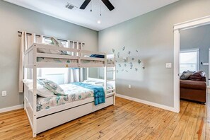Una habitación con literas, suelo de madera, una pared decorada con vinilos y un sofá de cuero marrón en la habitación contigua.
