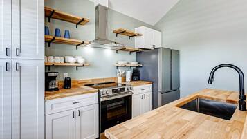 Una cocina moderna con armarios blancos, encimeras de madera, extractor de acero inoxidable, horno empotrado, refrigerador y grifo negro.