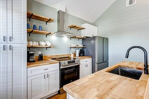 A modern kitchen with white cabinets, wooden countertops, a stainless steel range hood, a built-in oven, a refrigerator, and a black faucet. - Sea You Soon, Pet-Friendly | Community Amenities (Bolivar Peninsula)
