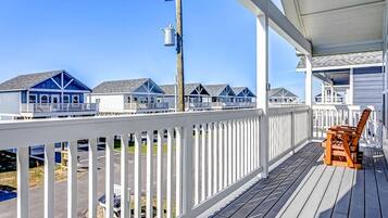 Une terrasse en bois avec une balustrade blanche, une chaise en bois et une vue sur les maisons de plage.