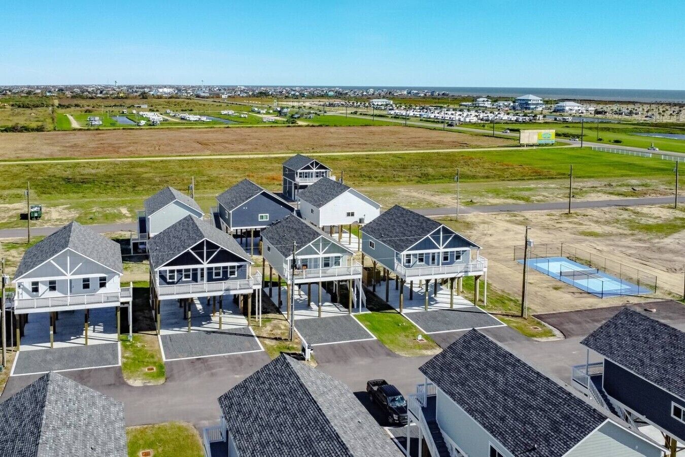 A coastal residential area with houses on stilts, a parking lot, and a view of the beach and ocean.