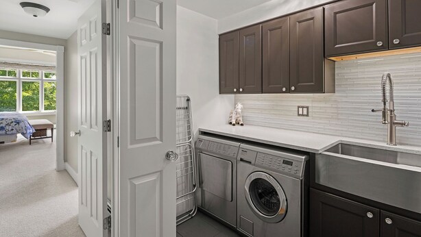 Una cocina moderna con lavadora y secadora integradas, armarios de madera oscura y un salpicadero de azulejos blancos.