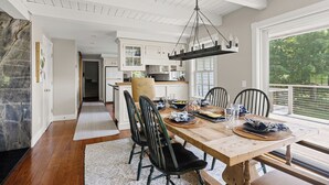 Comedor con mesa de madera dispuesta para cuatro, rodeada de sillas, y vista al exterior a través de amplias ventanas.