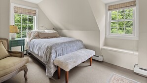 Un dormitorio con cama, una silla, una mesita de noche y una ventana con vista a la vegetación.