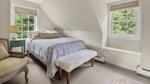 Ein Schlafzimmer mit einem Bett, einem Sessel, einem Nachttisch und einem Fenster mit Blick auf Grünflächen.