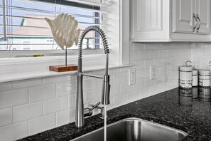 A kitchen with a stainless steel sink, a faucet with a flexible hose, and a window with blinds. - 3 Bd/2 Bth, Walkable to the Beach, Villa Verdie (Bolivar Peninsula)