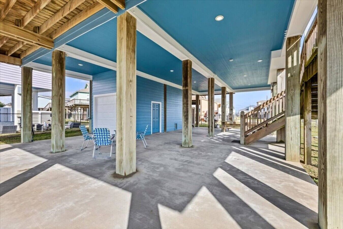 A covered outdoor area with concrete flooring, wooden columns, and a blue ceiling.