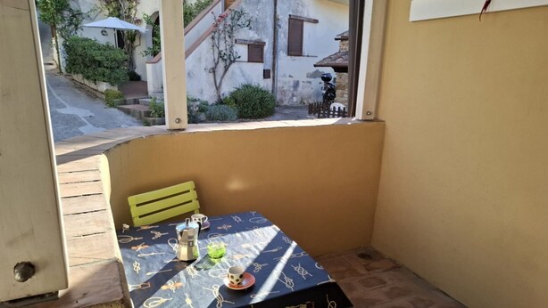 Ein kleiner Balkon mit Tisch und Stühlen, ein Fenster mit Blick auf eine Straße und eine Tür links.