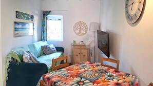 Ein Zimmer mit einem Bett, einem Tisch mit blumigem Tischläufer, einer Uhr und Bildern an der Wand.