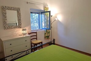 A bedroom with a bed, a dresser, a chair, a window with curtains, and a mirror. - Sighello Apartment (La Pila)