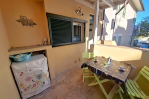A patio area with a table and chairs, a small window with shutters, and a decorative owl wall art. - Sighello Apartment (La Pila)
