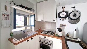 Eine kleine Küche mit Spüle, Herd, Backofen und einem Fenster mit Vorhängen.