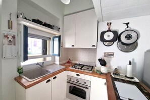 Eine kleine Küche mit Spüle, Herd, Backofen und einem Fenster mit Vorhängen.
