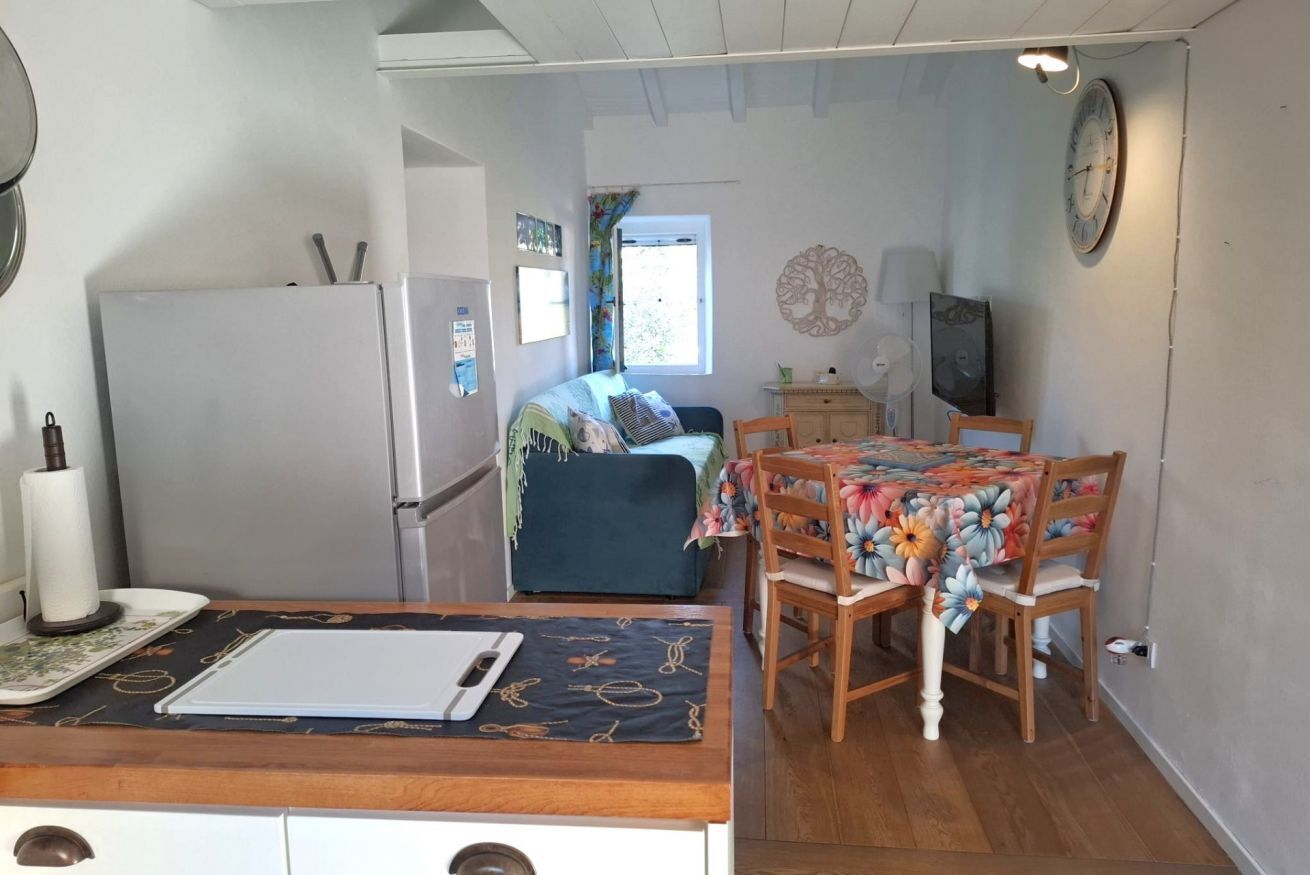 Un espacio habitable compacto con kitchenette, un área de comedor con mantel floral, una cama con cubrecama azul y un reloj de pared.