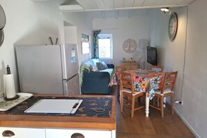 A compact living space with a kitchenette, a dining area with a floral tablecloth, a bed with a blue cover, and a wall clock. - Sighello Apartment (La Pila)