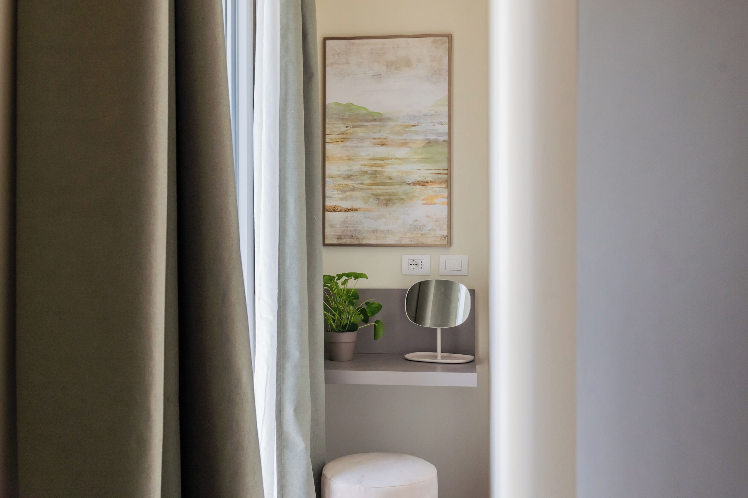 Ein Zimmer mit einem Gemälde, einem Blumentopf, einem Spiegel und einem Lichtschalter an der Wand.