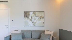 A neutral-colored sofa with cushions, a wall-mounted abstract painting, and a door with a light switch. - Circle - Erbonne - Two Bedroom Apartment, Sleeps 6 (Como)