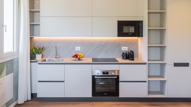 A compact kitchen with integrated appliances, including a microwave, oven, and dishwasher, with a marble backsplash and a fruit bowl on the counter. - Circle - Erbonne - Two Bedroom Apartment, Sleeps 6 (Como)
