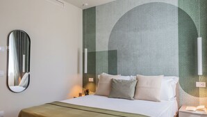 A hotel room with a bed, a bedside table with a book, a wall-mounted mirror, and a wall with a textured design. - Circle - Erbonne - Two Bedroom Apartment, Sleeps 6 (Como)