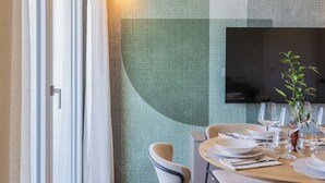 A dining area with a table set for two, a flat-screen TV mounted on the wall, and a window with curtains. - Circle - Erbonne - Two Bedroom Apartment, Sleeps 6 (Como)
