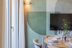 Un'area pranzo con un tavolo apparecchiato per due, una televisione a schermo piatto montata a parete e una finestra con tende.