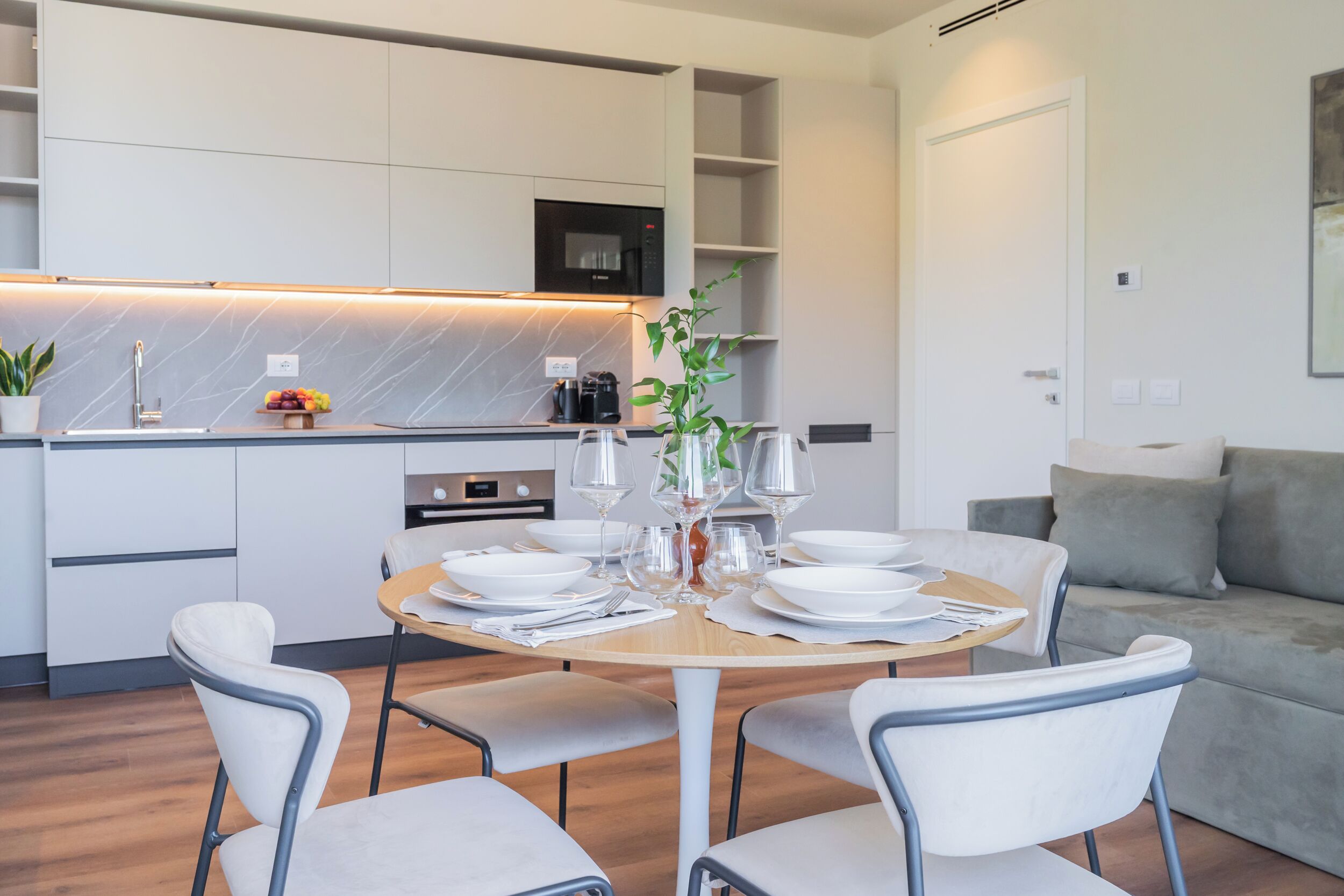 Una cucina moderna con mobili bianchi, un forno a microonde integrato e una ciotola di frutta sul bancone.