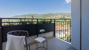 A balcony with a view of a hilly landscape, a chair, a small table with a book, and a towel. - Circle - Erbonne - Two Bedroom Apartment, Sleeps 6 (Como)