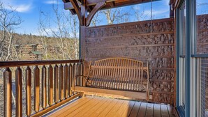 Una terraza de madera con una silla colgante, baranda de madera y vista a un paisaje montañoso.